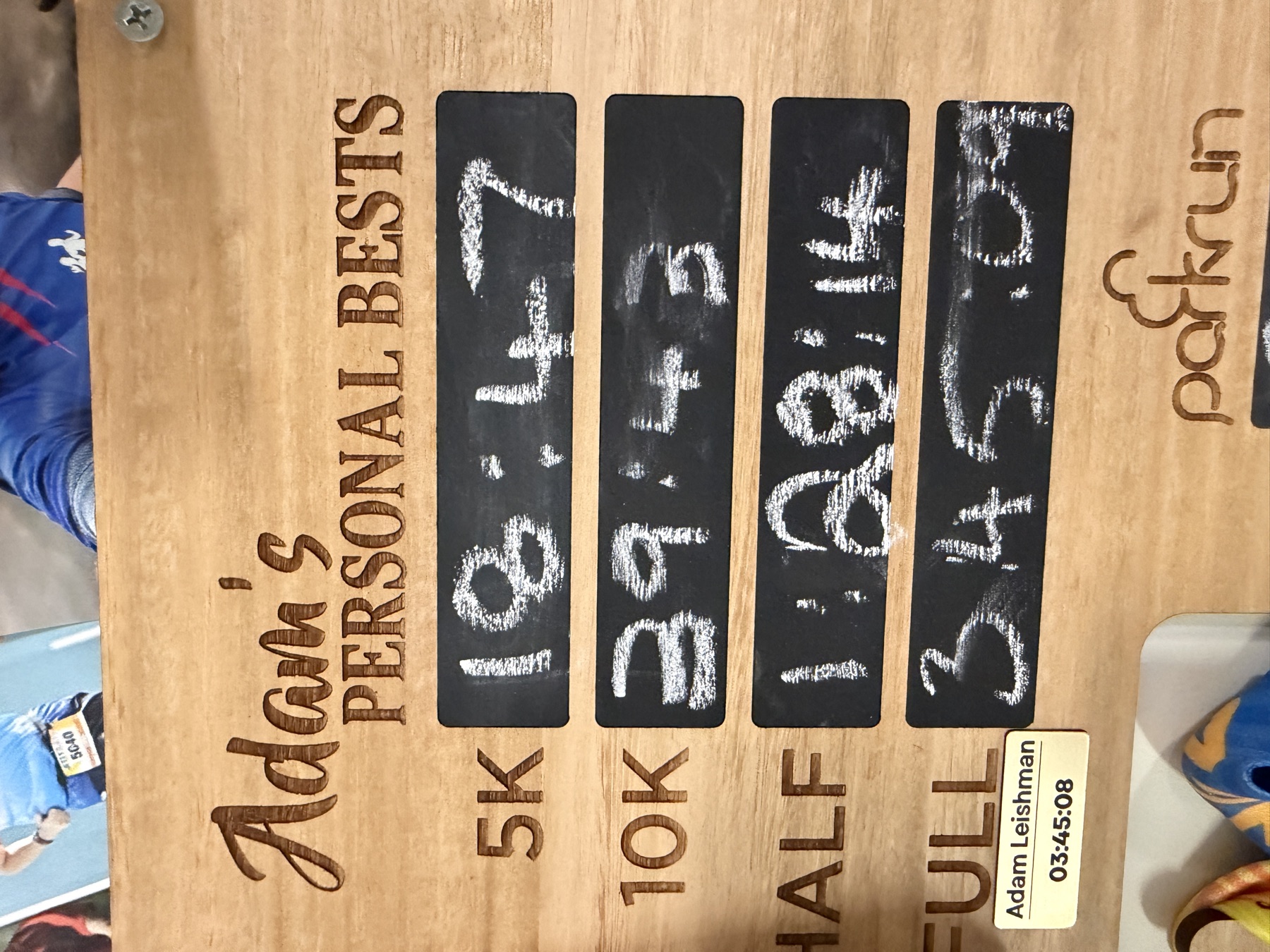 Adam's wooden personal-bests board with handwritten race times